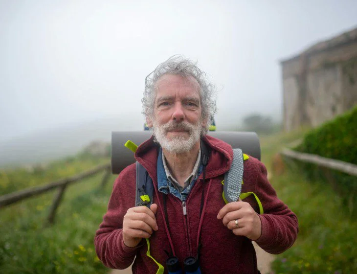 Man in a red jacket hiking outdoors on a foggy day.
