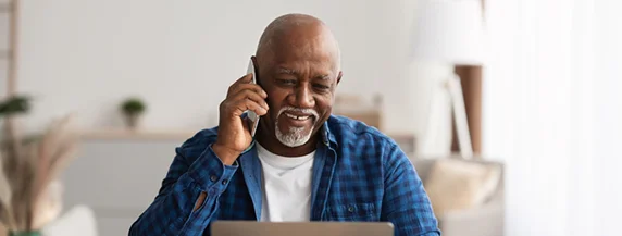 Man talking on phone while using a laptop at home.