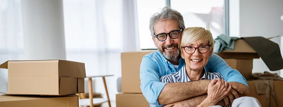 Smiling couple embracing in a room with moving boxes.