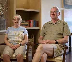 Two people sitting in a room with bookshelves in the background.