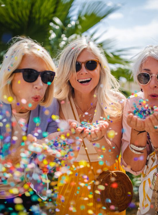 Fashionable mature friends having fun and celebrating by blowing colorful confetti in city street