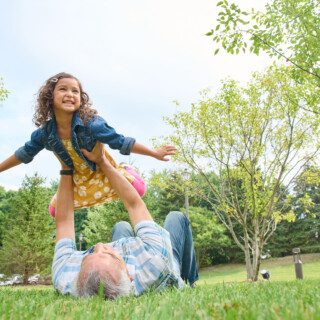 Man laying in grass holding granddaughter