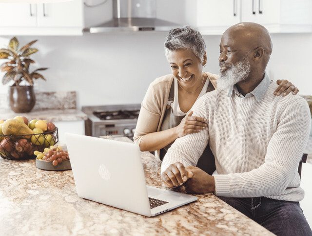 Happy senior couple browsing on the computer in their kitchen at home.