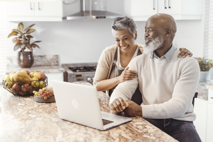 Happy senior couple browsing on the computer in their kitchen at home.