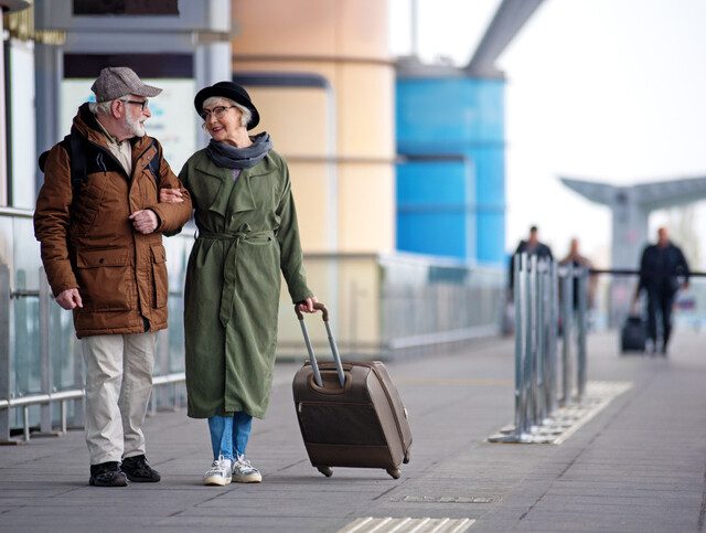 Older adult couple in winter coats standing outside airport.