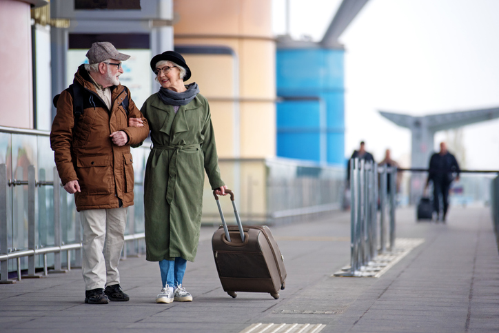 Older adult couple in winter coats standing outside airport.