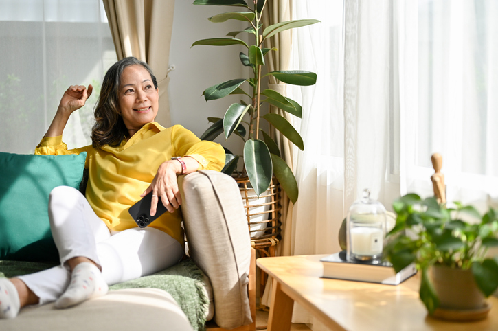 older adult woman smiling while sitting on the couch looking out the window